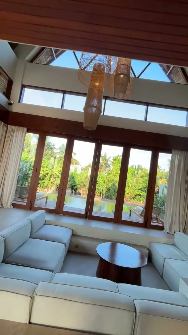 Photograph: the double-height living room of a finished hut, sofa and rattan pendants under the open gable
