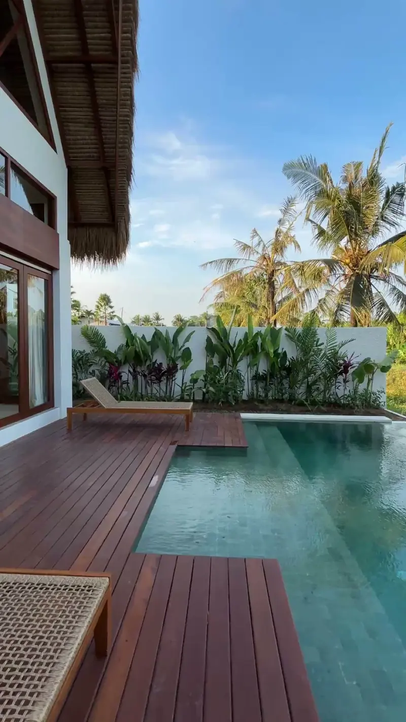 Photograph: the timber deck and the filled pool of a finished hut, loungers at the end and palms behind the wall