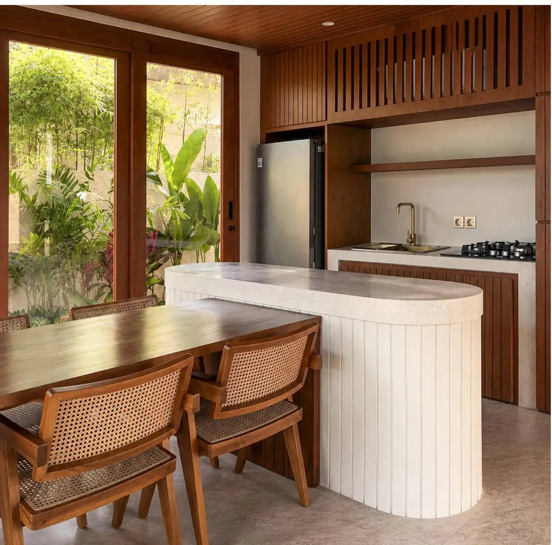 The kitchen counter running into the dining table, cane chairs, timber ceiling and garden through the glazing