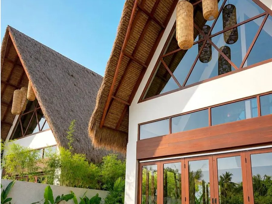 Luxury Huts &mdash; a row of thatched A&ndash;frame gables with timber&ndash;framed glazing against the sky
